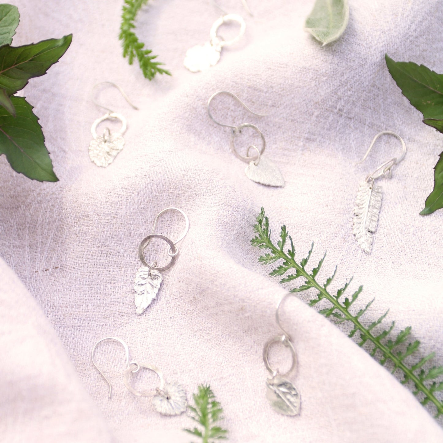 collection of fine silver herb charm earrings on linen background with herbs