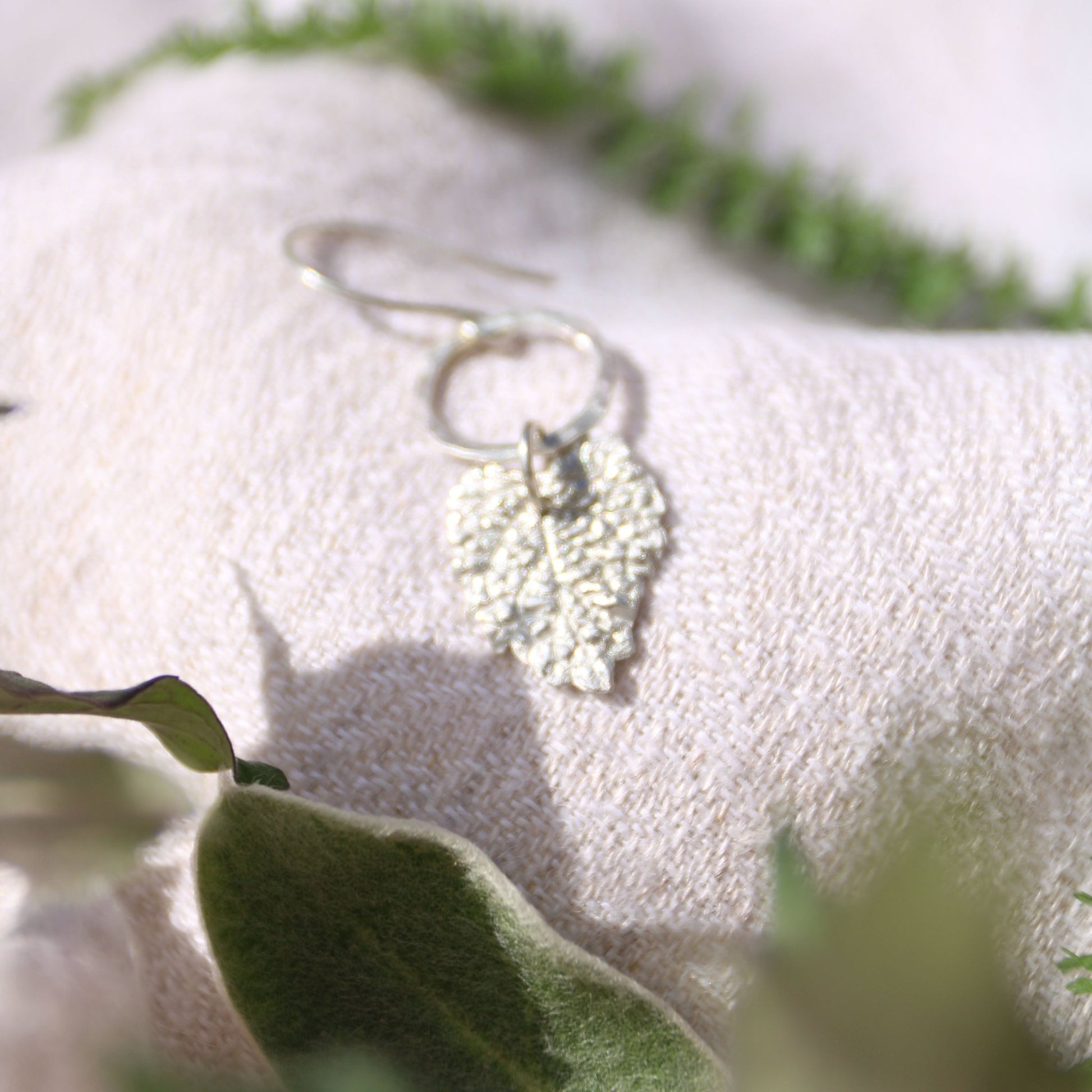 Lemon Balm fine silver herb charm earrings on a white fabric background with green herbs.