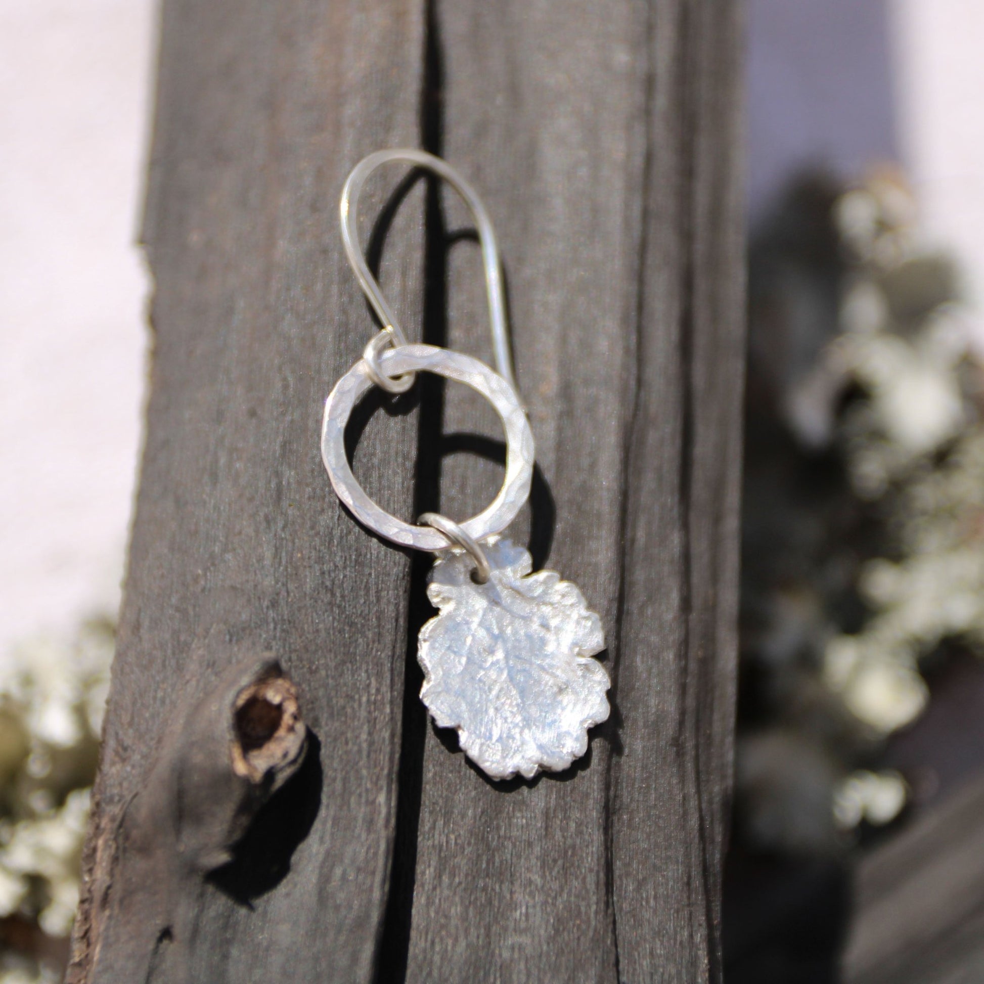 Silver earring with leaf-shaped pendant on wooden surface