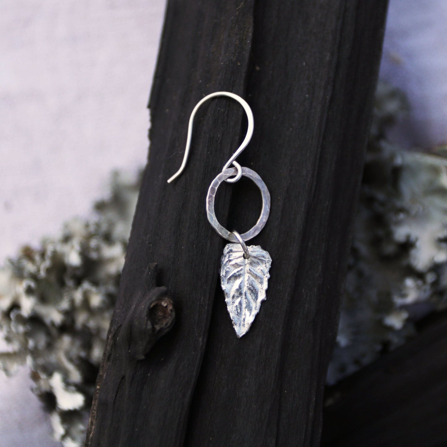 Silver leaf earring on a dark wooden surface with a natural background