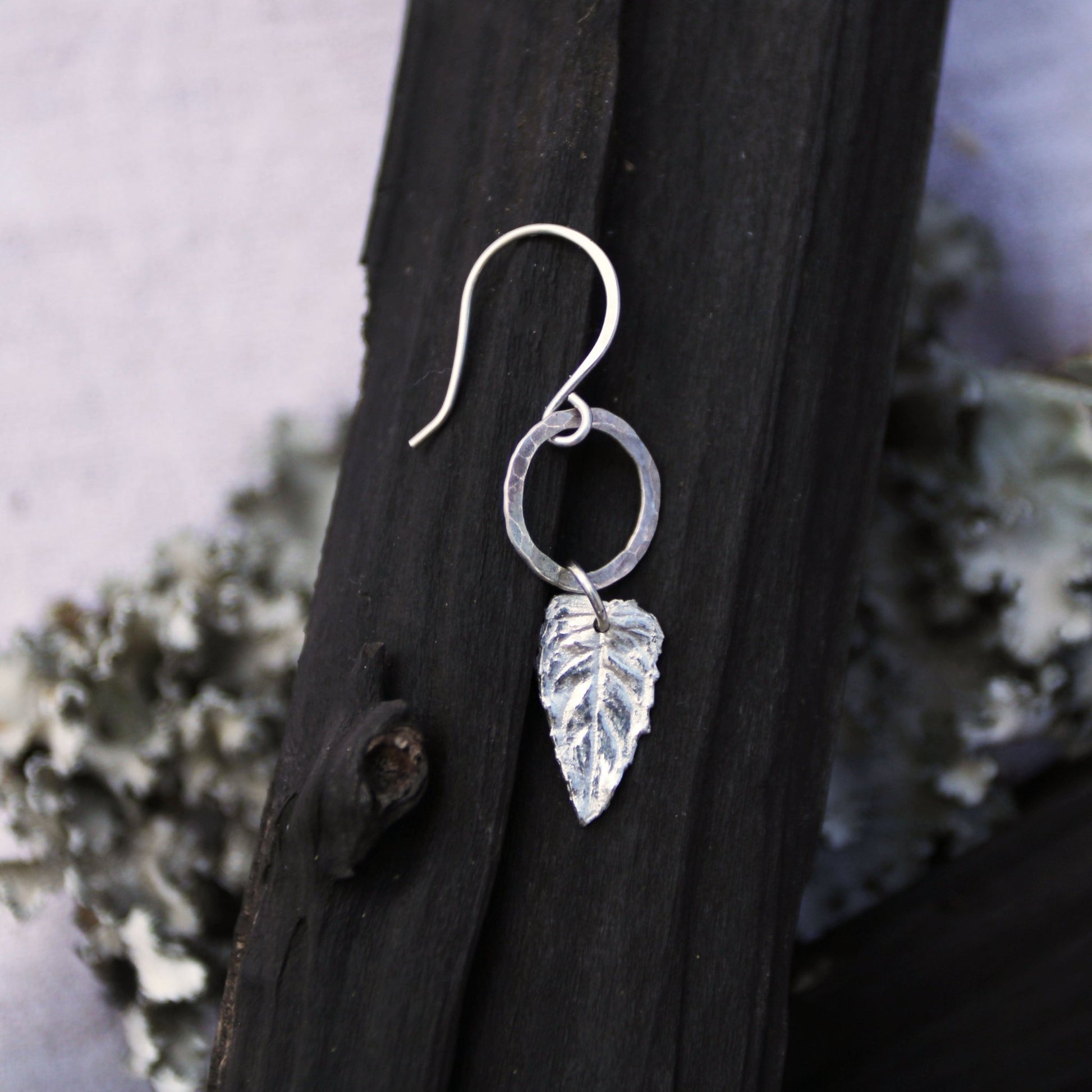 Silver leaf earring on a dark wooden surface with a natural background