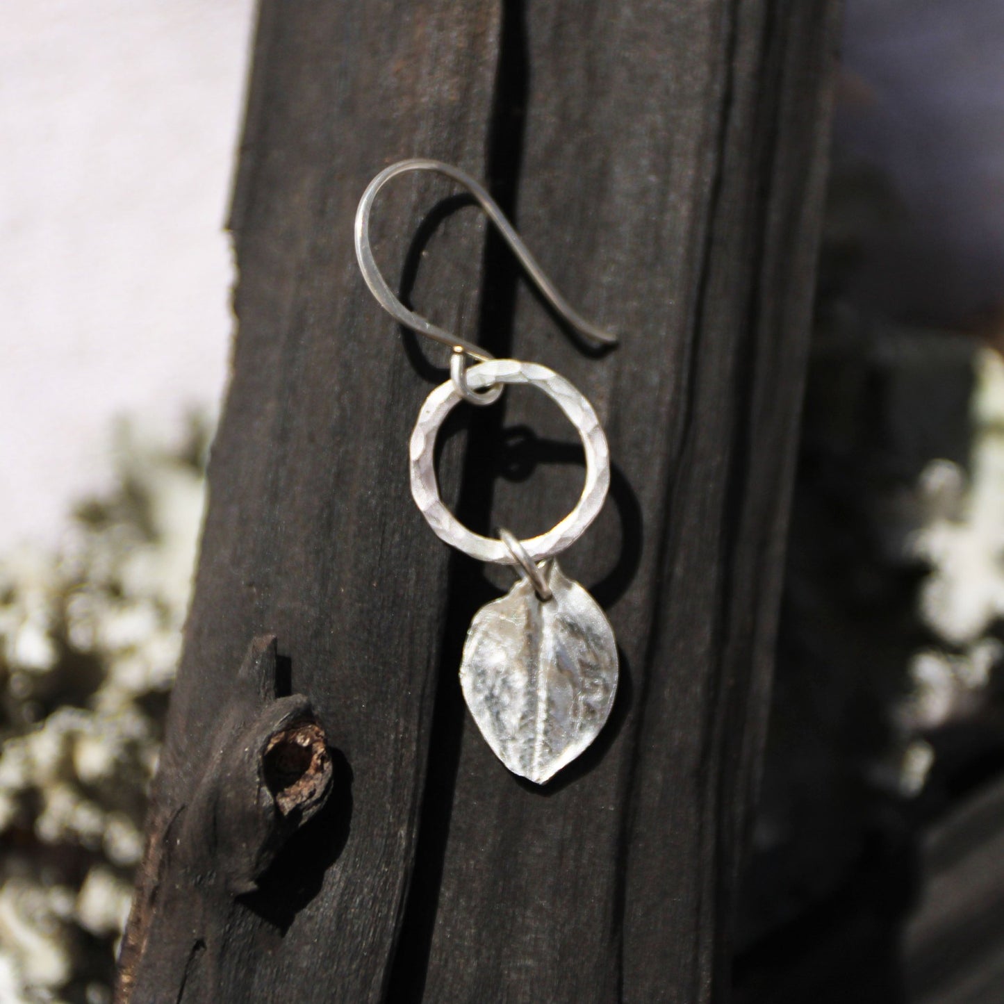 Echinacea Silver botanical earrings with leaf design hanging on a wooden surface.