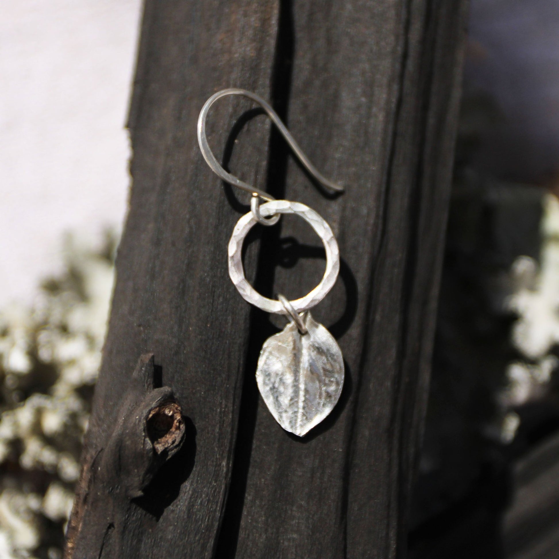 Echinacea Silver botanical earrings with leaf design hanging on a wooden surface.