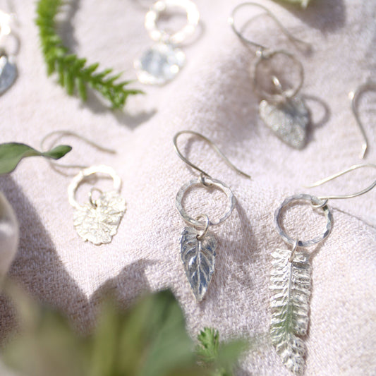 Silver leaf earrings on a textured surface with greenery
