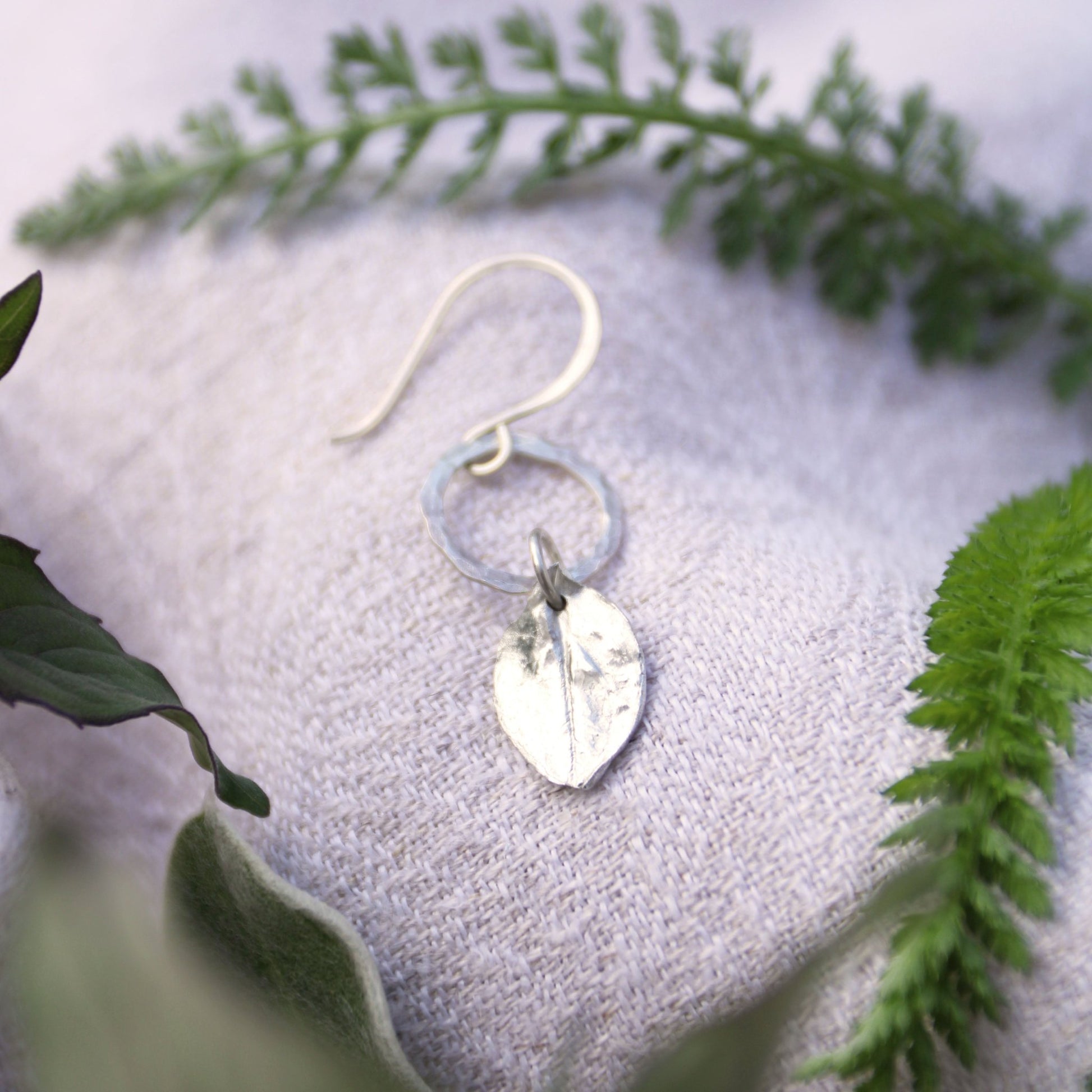 Echinacea fine silver herb charm earring on a textured surface with green herbs in the background