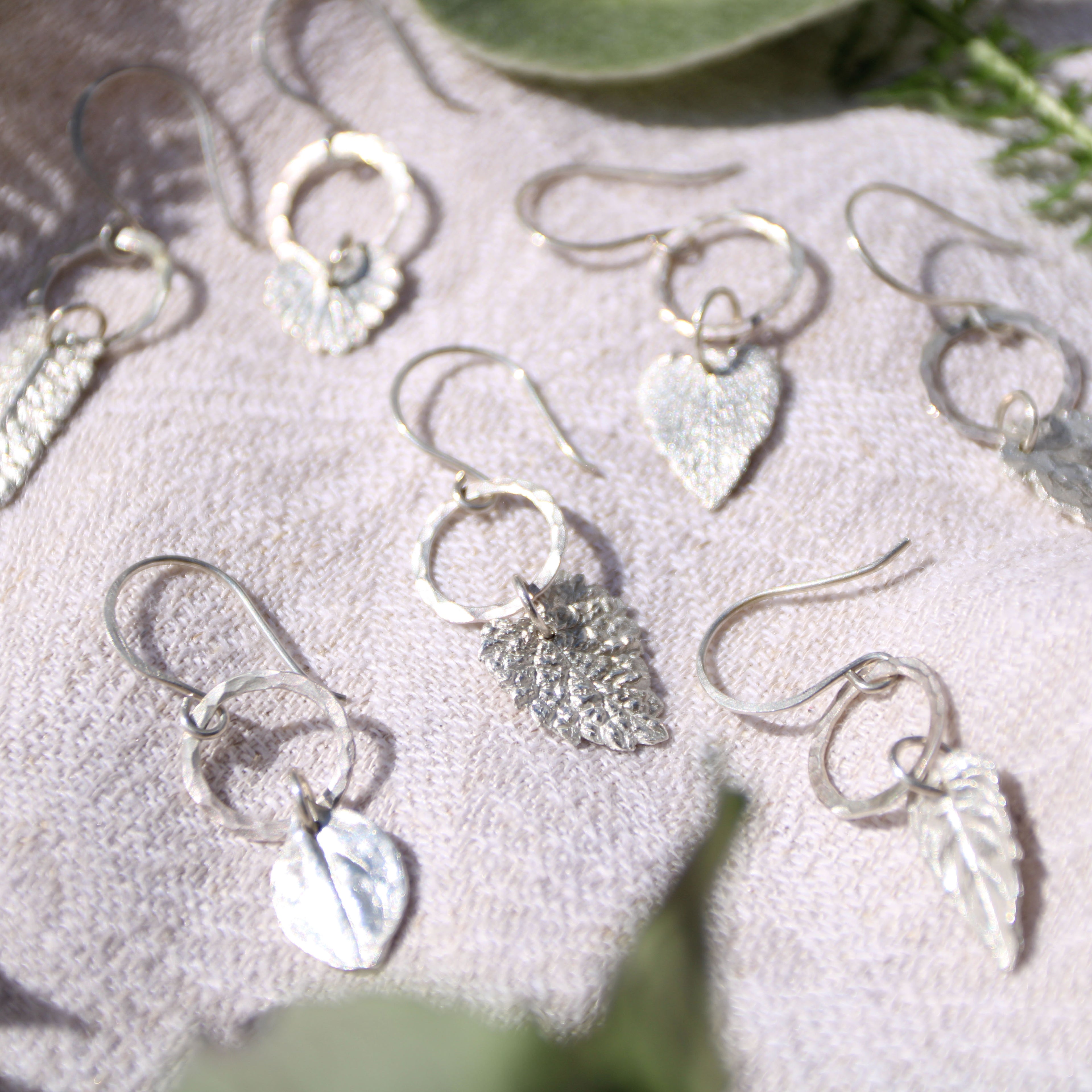 Silver earrings with leaf-shaped charms on a textured surface