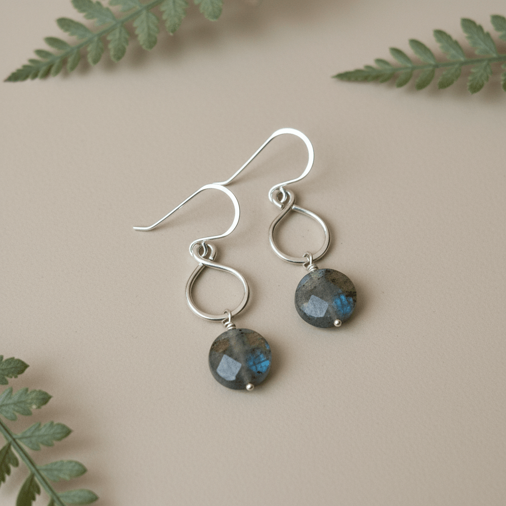 Silver earrings with gemstones on a beige background with green leaves
