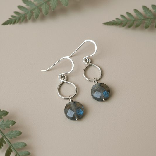 Silver earrings with gemstones on a beige background with green leaves