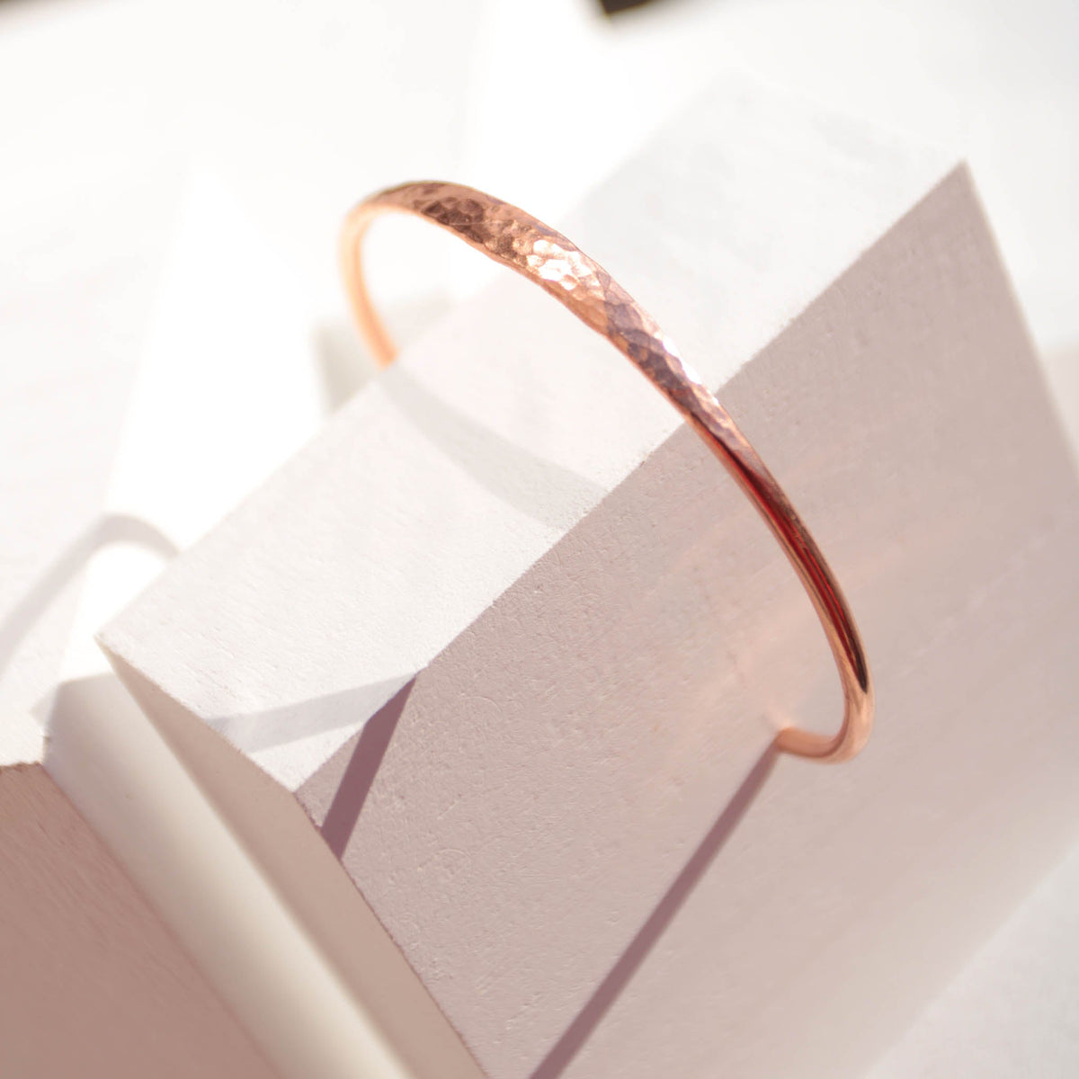 Minimalist hammered copper cuff bracelet with a reflective texture and warm golden glow