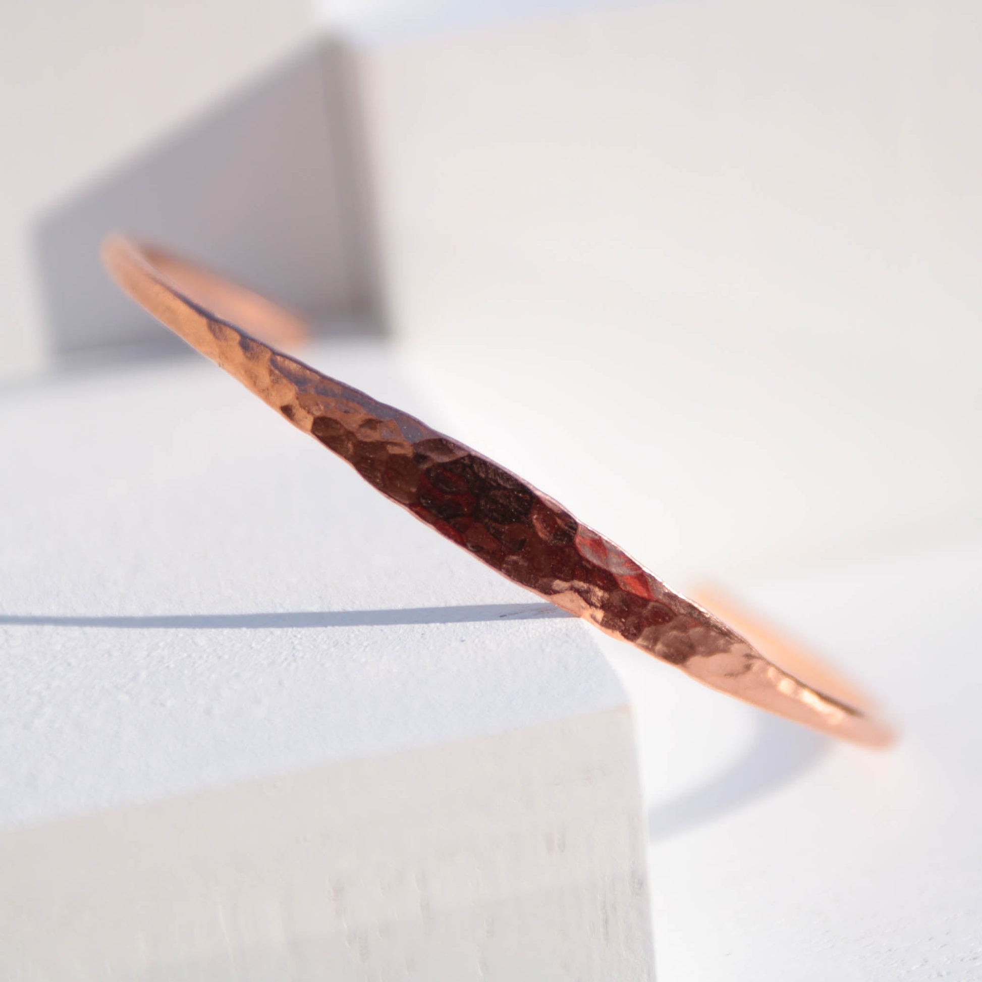 Minimalist hammered copper cuff bracelet with a reflective texture and warm golden glow
