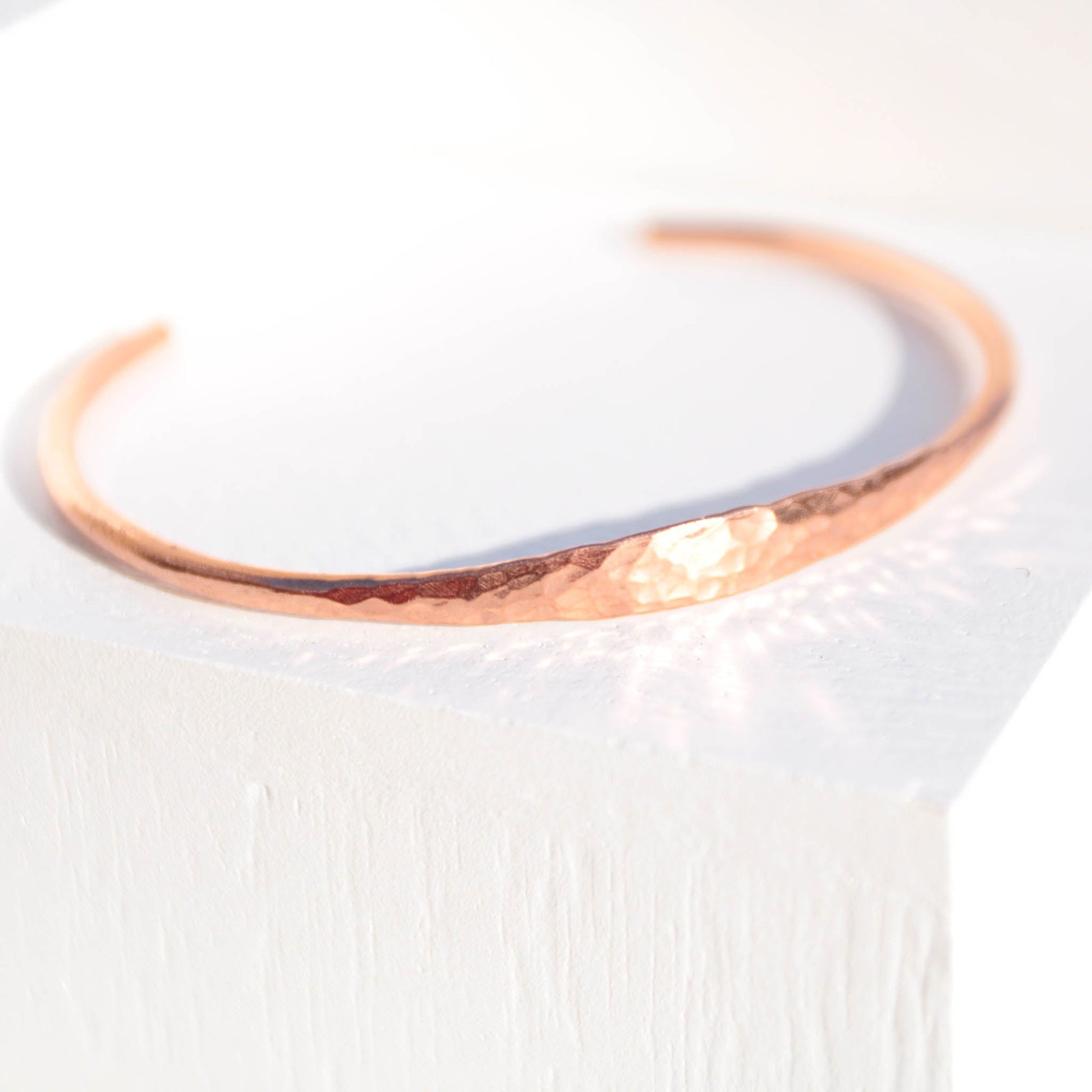 Minimalist hammered copper cuff bracelet with a reflective texture and warm golden glow