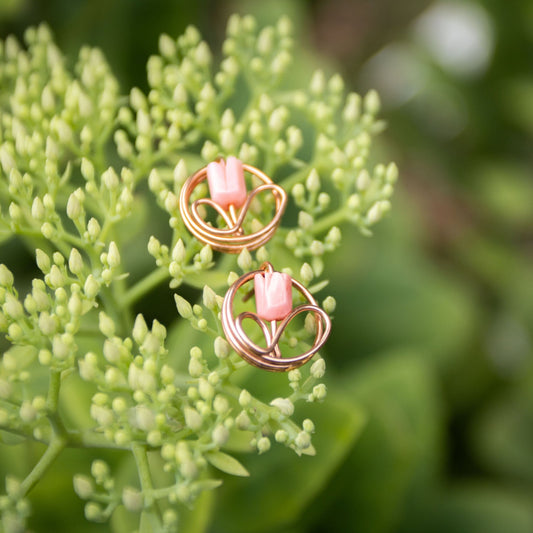 Copper wire wrapped flower bud pendant earrings on mossy rock in dappled sunlight